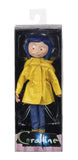 "Figura de acción Coraline NECA de 7 pulgadas en su empaque original, mostrando el diseño detallado del personaje con su característico impermeable amarillo."